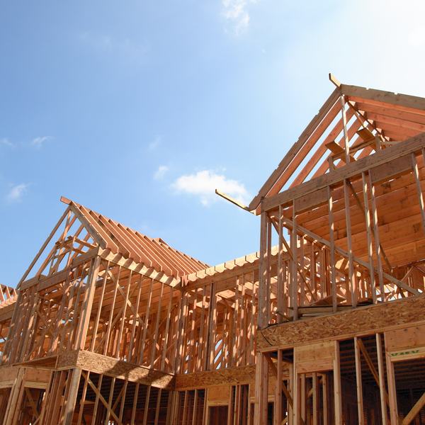 Wooden frames of a new building under construction, with open skeletal structures against a clear blue sky.